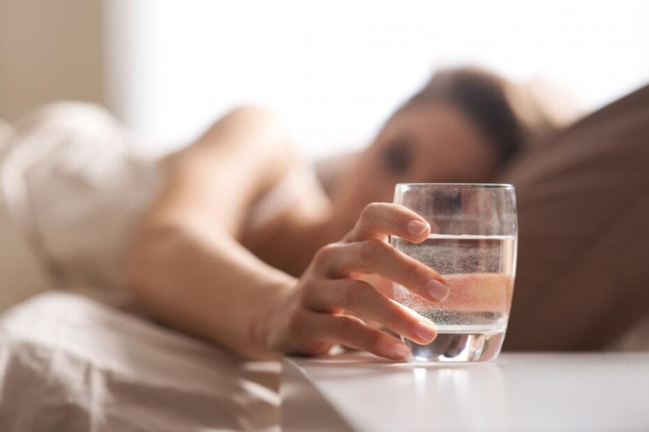woman in bed reaching for glass of water to drink before going to sleep